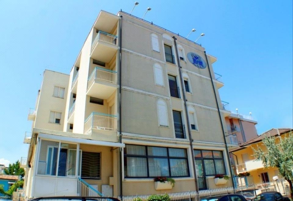 a beige apartment building with balconies , surrounded by cars parked in front of it under a clear blue sky at Hotel Jasmine