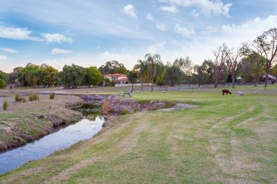 a golf course with a small creek , grass , and trees , as well as a house in the background at The Swan Valley Retreat