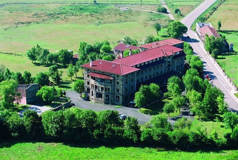 aerial view of a large stone building surrounded by green grass and trees , located in the countryside at Balneario de Corconte