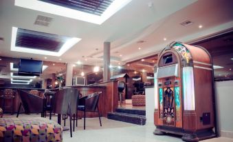 a room with a jukebox in the corner , surrounded by chairs and tables , and a bar area at El Paseo Hotel