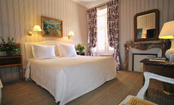 a well - decorated hotel room with a large bed , white linens , and a fireplace , along with other amenities at Chateau de la Bourdaisiere