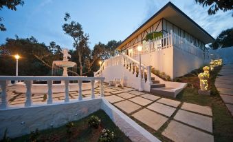 a large white house surrounded by trees and grass , with a staircase leading up to the entrance at Bilut Hills @ Bentong