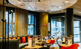 a modern lounge area with a large paper ceiling , black and red chairs , and a bicycle decoration at Ibis de Panne