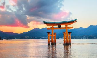 a large , orange torii gate stands in the water with a beautiful mountain range in the background at Sakuraya