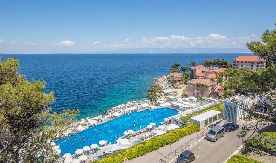 a large swimming pool is surrounded by lounge chairs and umbrellas in a resort area with the ocean visible in the background at Vitality Hotel Punta