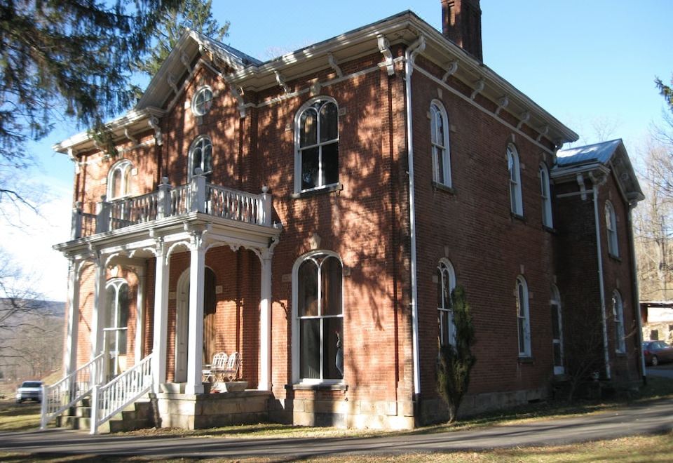 a red brick house with white trim and a porch , surrounded by trees and grass at Shaw Mansion Inn