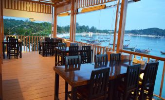 a wooden dining area with tables and chairs , overlooking a body of water with boats at Chareena Hill Beach Resort