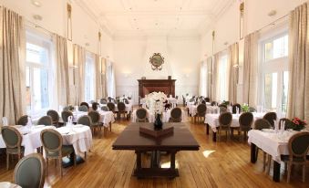 a large , elegant dining room with wooden floors , white walls , and multiple tables set for dinner service at Hôtel du Parc