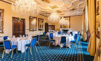 a formal dining room with blue and white chairs and tables , chandeliers hanging from the ceiling at Dalhousie Castle Hotel