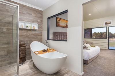 a modern bathroom with a freestanding bathtub , wooden floors , and a large mirror reflecting the bedroom at The Swan Valley Retreat