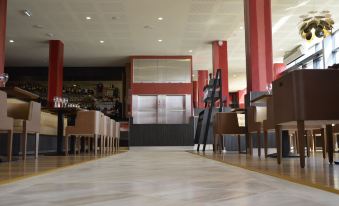 a long dining area with wooden tables and chairs , red pillars , and a large screen on the wall at Le Grand Hotel