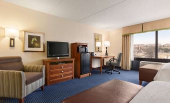 a hotel room with a bed , desk , and television , along with a view of the city through large windows at Hampton Inn Warrenton, VA