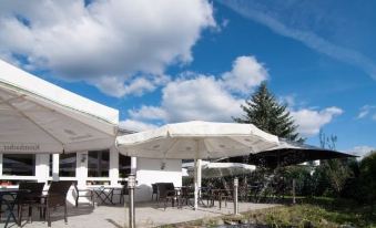 a patio area with tables , chairs , and an umbrella in front of a building under a blue sky at Lotus