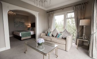 a modern living room with a beige couch , glass coffee table , and large windows leading to an outdoor area at Clanard Court Hotel