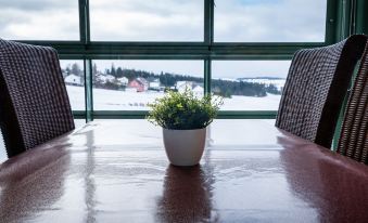 a wooden table with two chairs and a potted plant in front of a window overlooking a snowy landscape at B 94