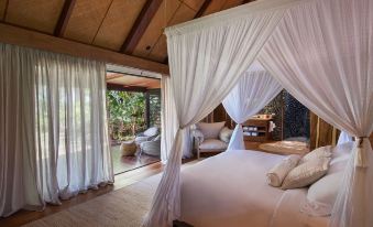 a luxurious bedroom with a canopy bed , white curtains , and a view of a dining area at The Wakaya Club & Spa