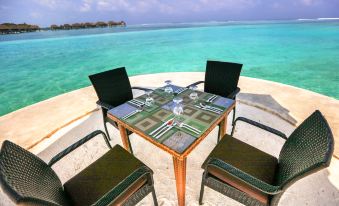 a wooden table with chairs on a balcony overlooking the ocean , creating a serene atmosphere at Pearl Sands of Maldives