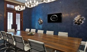 a conference room with a wooden table and chairs , a tv on the wall , and chandeliers hanging from the ceiling at The Pearl Hotel