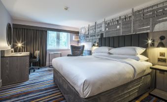 a large bed with white linens is in a hotel room with a striped rug and a window at DoubleTree by Hilton Bristol South - Cadbury House