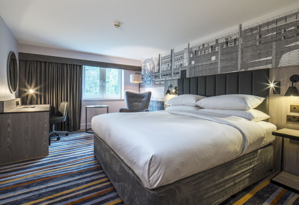 a large bed with white linens is in a room with a window , chair , and striped carpet at DoubleTree by Hilton Bristol South - Cadbury House