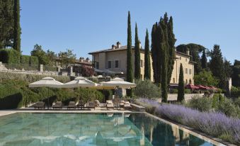 a large outdoor pool surrounded by a lush garden , with several lounge chairs and umbrellas placed around the pool area at Rosewood Castiglion del Bosco