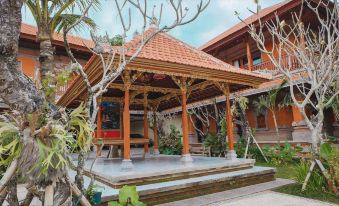 a wooden gazebo with a thatched roof , surrounded by lush greenery and a pool , under a clear blue sky at Ubud Hotel & Cottages