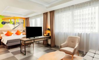 a hotel room with a large flat - screen tv mounted on the wall , a comfortable chair , and a dining table at Ibis Styles Bekasi Jatibening