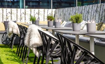 a row of black and white chairs is arranged outside on a grassy patio , surrounded by potted plants at Radisson Blu Hotel Uppsala