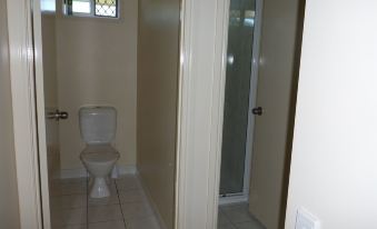 a small , empty bathroom with white walls and floor , a toilet , and a shower door at Emu Park Motel