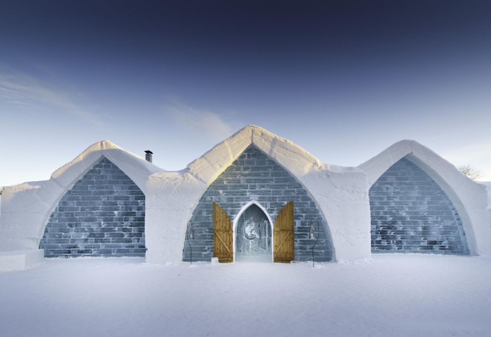 a large , snow - covered building with a blue and white exterior and a door , surrounded by snow at Hotel de Glace (Ice Hotel)