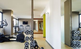 a gym with various exercise equipment , including weights and mats , in a spacious room with white walls at Mercure Milano Agrate Brianza