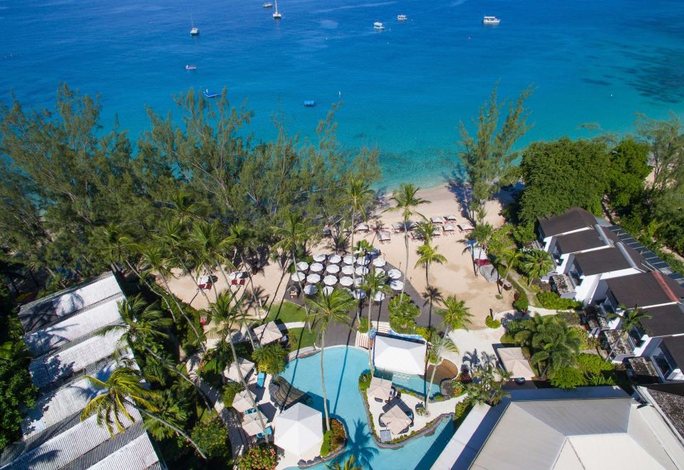 aerial view of a beachfront resort with umbrellas , palm trees , and a pool , overlooking the ocean at Colony Club by Elegant Hotels