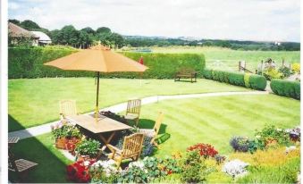 a backyard with a table , chairs , and an umbrella set up for outdoor dining , surrounded by green grass and flowers at Ashcroft Farmhouse