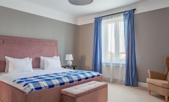 a large bed with a pink headboard and blue and white striped blanket is in a room with a chair , lamp , and window at MillCreek