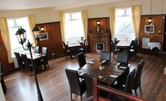 a large dining room with wooden tables and chairs , a fireplace , and yellow curtains near the windows at The Moorland Hotel