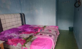 a bed with pink and purple bedding is in a room with blue walls and green tile floor at Penginapan Rindu Alam Soala Gogo