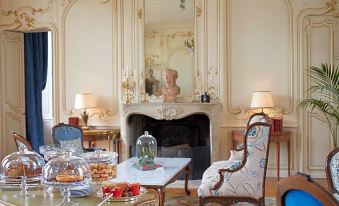a living room with a fireplace , dining table , chairs , and a statue of a woman at Chateau d'Audrieu