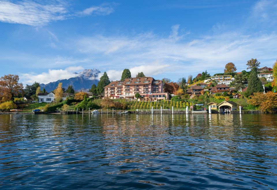 a picturesque view of a lake with a hotel on an island , surrounded by mountains and trees at Seehotel Kastanienbaum