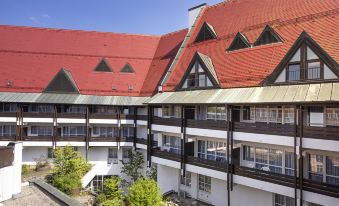 a red - roofed apartment building with white balconies and windows , surrounded by trees and a blue sky at Achat Hotel Kaiserhof Landshut