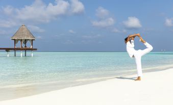 a woman in a white outfit is doing a yoga pose on the beach with a white gazebo in the background at Anantara Dhigu Maldives Resort