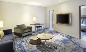 a living room with a blue and white patterned carpet , a couch , a chair , and a television at Novotel Jakarta Mangga Dua Square