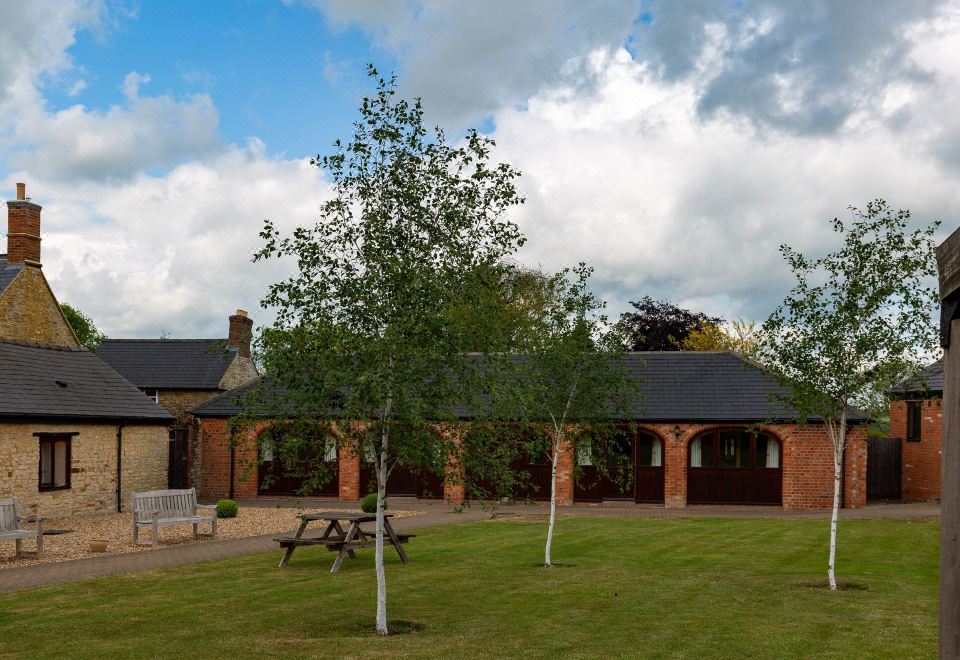 a brick house surrounded by green grass and trees , with a picnic table in the yard at Church Farm Lodge