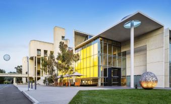 a modern building with a yellow facade and large windows is surrounded by green grass and trees at Hyatt Hotel Canberra - A Park Hyatt Hotel