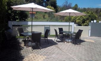 a patio with several chairs and umbrellas set up for outdoor dining , surrounded by trees at Milos Apartments