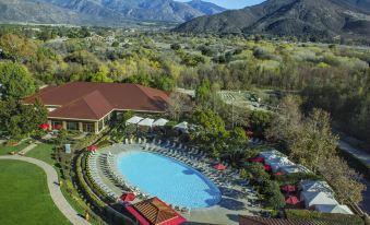aerial view of a resort with a large pool surrounded by lounge chairs , umbrellas , and a mountain in the background at Pala Casino Spa and Resort
