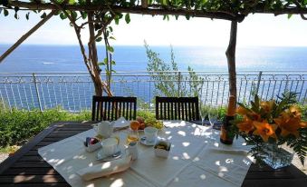 a dining table set with a plate of food , a cup , and a bottle of wine , situated on a balcony overlooking the ocean at Villa Maria