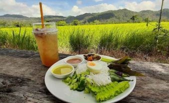 a plate of food and a glass of iced tea are placed on a wooden table in front of a scenic view at Payabangsa Resort