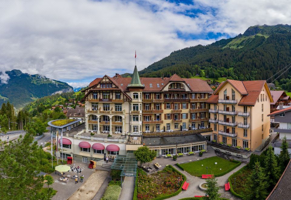 an aerial view of a large hotel surrounded by greenery , with mountains in the background at Arenas Resort Victoria-Lauberhorn