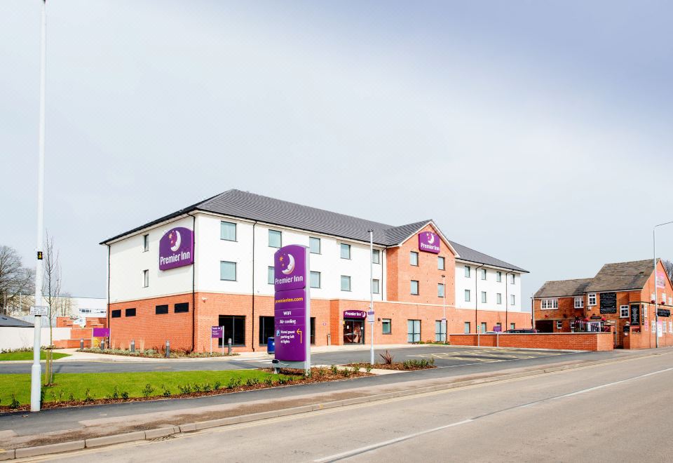 a large , modern hotel building with a purple sign and a road in front of it at Premier Inn Melton Mowbray