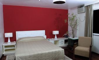 a bedroom with a red wall , a bed , and a tv . also a chair in the room at Hotel du Lac Macae